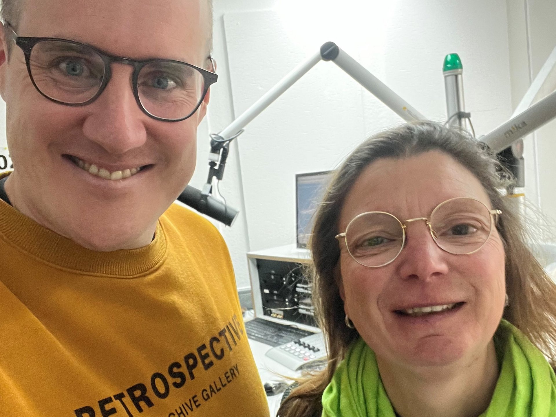 rechts steht ein Mann, links eine Frau, im Hintergrund das Studio
